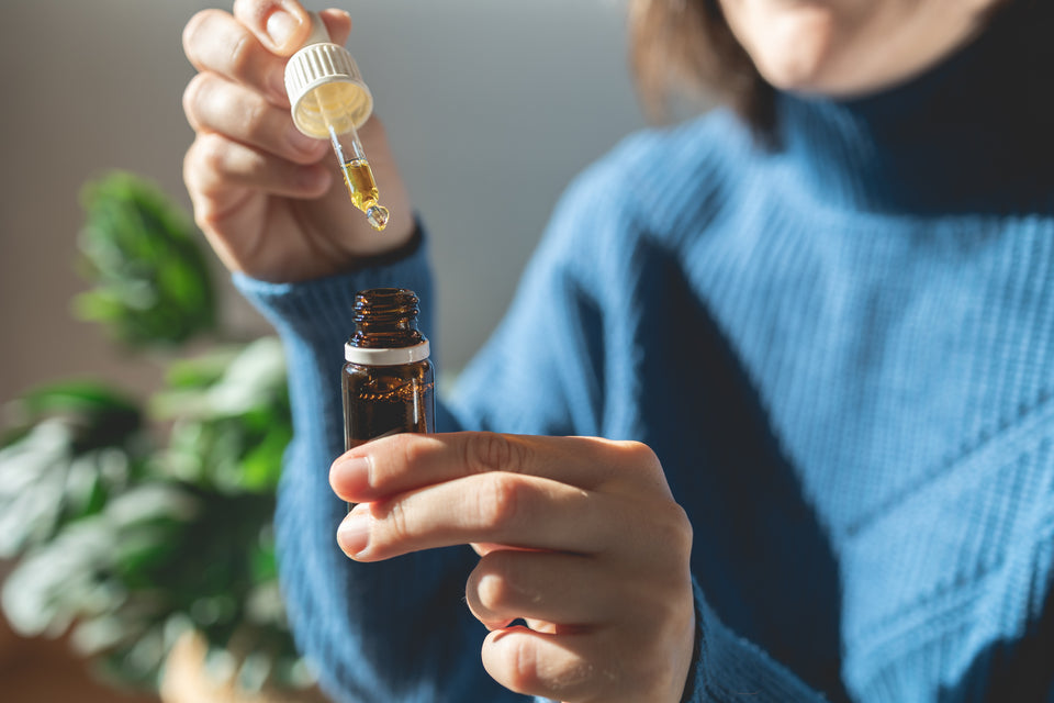 A woman holding a bottle of CBD oil and a dropper, getting ready to use it as a part of her daily skincare routine.